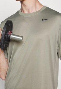 Camiseta Nike de color verde oliva, hecha de tela suave, con cuello redondo, mangas cortas y un logo de swoosh negro en el pecho.