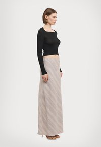 Black ribbed long-sleeve top paired with a beige skirt featuring diagonal stripes and a soft texture, complemented by open-toe heeled sandals.