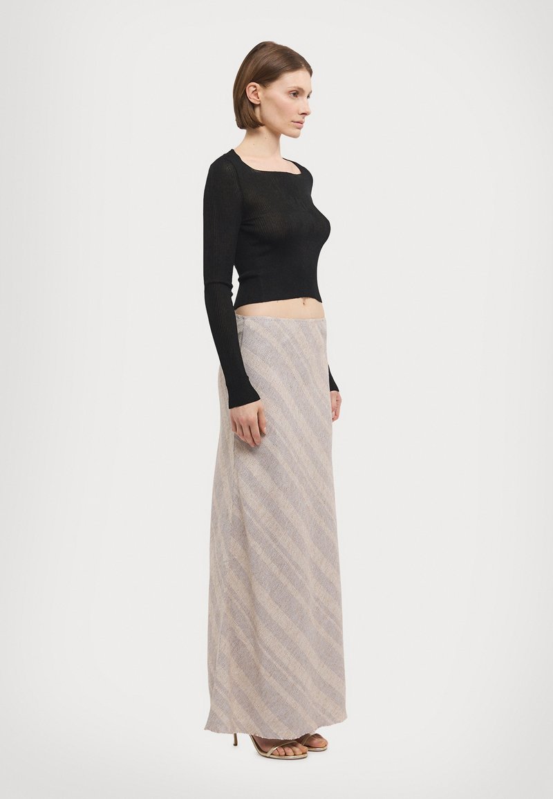 Black ribbed long-sleeve top paired with a beige skirt featuring diagonal stripes and a soft texture, complemented by open-toe heeled sandals.