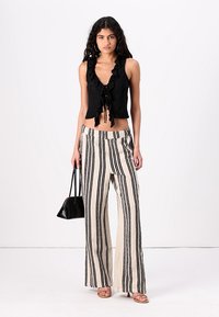 Black cropped top with ruffles, paired with high-waisted wide-leg pants featuring a vertical black and cream stripe pattern. Black handbag and sandals.