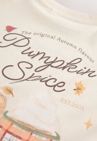 Texto que dice "The original Autumn flavour Pumpkin Spice EST. 2003" con hojas de otoño y una ilustración de un postre cubierto con nata montada sobre tela.