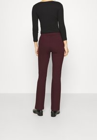 Pantalons évasés bordeaux en tissu extensible, avec une taille haute et une texture lisse, associés à un haut ajusté à manches longues noir.