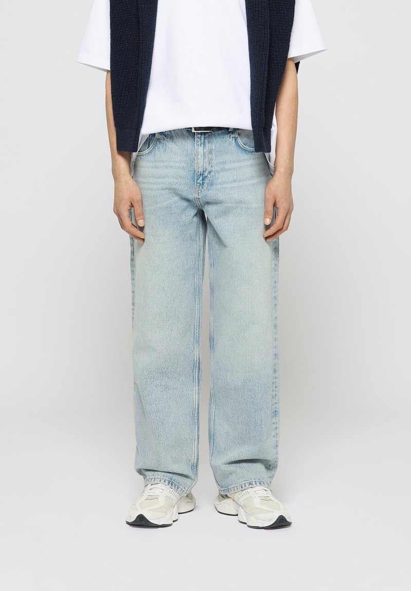 Helle, locker sitzende Denim-Jeans in Blau mit einem ausgewaschenen Design, geradem Bein, fünf Taschen und einem mittelhohen Bund, getragen mit einem weißen T-Shirt.