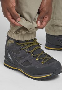 Schwarze Wanderschuhe mit gelben Akzenten, aus Wildleder und Mesh, mit strapazierfähigen Schnürsenkeln und einer strukturierten Gummisohle. Die Hose hat elastische Bündchen.