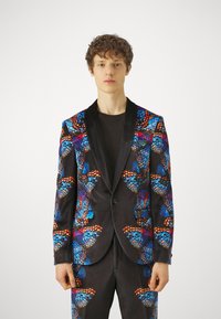Svart blazer med et livlig sommerfugl-mønster i blått, oransje og rødt. Blazeren har satengslipper og knapplukking.