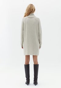 Vestido de punto acanalado gris claro con un alto cuello de tortuga. Presenta mangas largas y un corte relajado, terminando por encima de las rodillas.