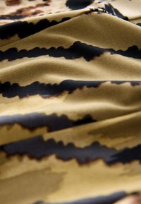 Tessuto decorato con texture liscia, con strisce ondulate nere e marroni su uno sfondo beige dorato. Aspetto leggermente stropicciato.