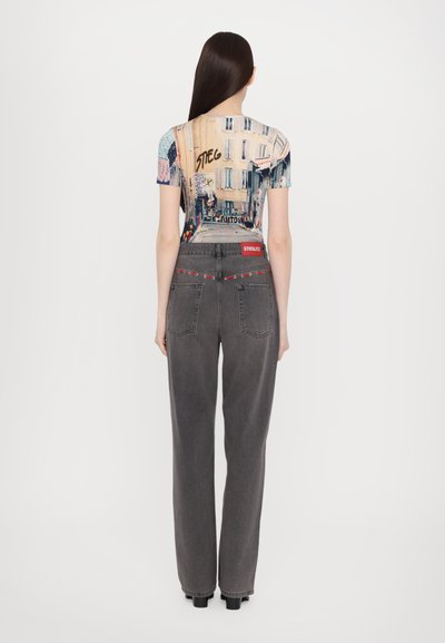 Fitted graphic t-shirt with urban art print, paired with high-waisted, loose-fit gray denim jeans with red stitching and logo on the waistband.