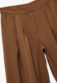 Pantalones plisados marrones hechos de una tela ligera y arrugada. Cuentan con una cintura suave y bolsillos laterales, con un corte relajado a lo largo de las piernas.