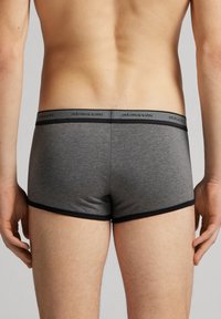 Grå bomullsboxer med en svart midja som visar varumärkesnamnet. Tyget är mjukt och passformen är tät med en minimal design.