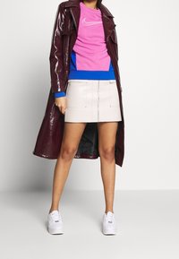 Burgundy patent leather long coat, pink and blue Nike sweatshirt, beige mini skirt with vertical zipper, white sneakers.