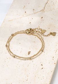 Pulsera de cadena de oro que presenta dos hebras finas con pequeñas cuentas redondas, un cierre tipo langosta y dos acentos en forma de corazón. Superficie texturizada.