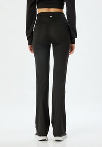 Zwarte flared broek gemaakt van rekbaar materiaal, met een hoge taille en een klein logo op de achterkant. Soepele textuur en nauwkeurige pasvorm.