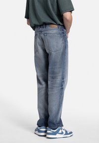 Jeans din denim de culoare albastră deschisă, cu o croială relaxată, având talie medie, două buzunare dorsale și accente uzate distorsionate. Asortați cu adidași albaștri.