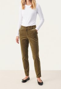 Pantaloni in velluto a coste verde oliva con una vestibilità affusolata, caratterizzati da due tasche frontali e una vita liscia, abbinati a una maglietta bianca a maniche lunghe.