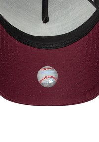 Cappellino di baseball bordeaux con visiera nera; include un adesivo circolare del logo MLB con un design di baseball sul lato interno della visiera.