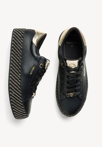 Baskets plateformes noires avec semelles épaisses tissées à motif, accents dorés au talon et à la languette, lacets noirs et détails métalliques de la marque.