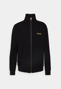 Svart zip-up jacka i mjukt material, med hög krage, fickor fram och en gyllene "BOSS"-logotyp på bröstet.
