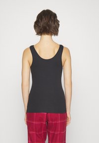 Svart tanktop med utringet rygg og brede stropper, laget av glatt stoff, kombinert med røde og rosa rutete pysjbukser.