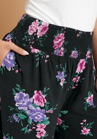 Svarta blomsterbyxor med smockad midja, prydda med lila och rosa blommor, i mjukt tyg och med sidfickor.