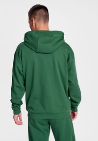 Grön hoodie i mjukt material, med en stor huva, långa ärmar och ribbade muddar, i en avslappnad passform.