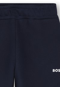 Joggings bleu marine en tissu doux, dotés d'une taille élastique et d'un logo imprimé blanc sur le bas de la jambe. Texture lisse, sans motifs.