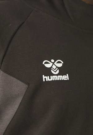 Tissu noir montrant un logo d'abeille stylisée blanche avec le mot « hummel » en dessous.