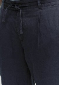 Navy linnen broek met een relaxte pasvorm, voorzien van een striksluiting, zijzakken en een subtiele textuur.