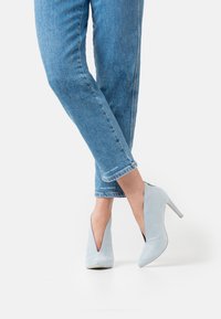 Escarpins bleu clair à bout pointu et design en V profond. Fabriqués en daim, avec un talon aiguille fine. Les jeans ont une longueur raccourcie.