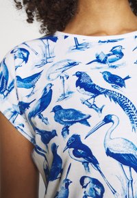 Cotton t-shirt with short sleeves featuring a blue bird print against a white background. Various bird species depicted in a detailed, stylized design.