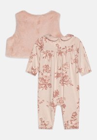 Rosa fuskpälsväst i kombination med en långärmad jumpsuit med ett blommönster i dämpade rosa nyanser på en beige bakgrund. Knäppning bak.