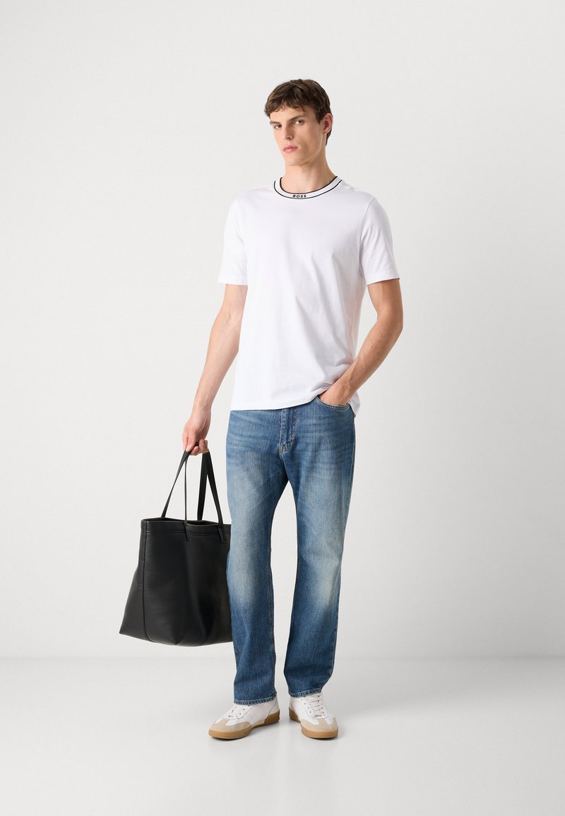 Weißes T-Shirt mit kurzen Ärmeln und schwarzem Kragen, blaue Jeans im Denim-Stil und eine schwarze Ledertasche, kombiniert mit weißen Sneakern.