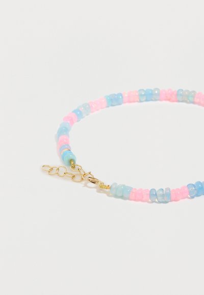Βραχιόλι με εναλλασσόμενες παστέλ ροζ και μπλε διάφανες χάντρες και ρυθμιζόμενο κούμπωμα σε χρυσό τόνο σε λευκό φόντο.