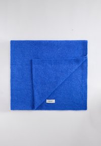 Blue blanket made of soft fabric, featuring a folded corner and a brand label. Textured surface, sleek design, and uniform color.