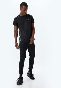 Sort atletisk T-shirt med korte ærmer, prydet med subtile grå sideakcenter. Sammen med sorte joggerbukser og sorte sneakers.