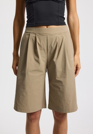 Pantaloncini beige fino al ginocchio realizzati in tessuto leggero, caratterizzati da pieghe in vita e una fascia piatta in vita, con un dettaglio di branding sottile.