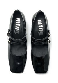 Des chaussures Mary Jane noires en cuir verni avec un bout carré, deux brides avec boucles, et une texture lisse et brillante sur les semelles intérieures.