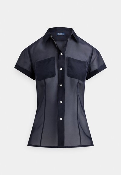 Tumši zila īsām piedurknēm caurspīdīga pogājama krekls ar divām krūšu kabatām un smailu apkakli, kas parāda pieguļošu siluetu.