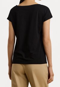 Czarny t-shirt z krótkim rękawem i szerokim dekoltem, wykonany z miękkiego materiału. Tył ma luźniejszy krój, z czystymi szwami i bez widocznych metek.