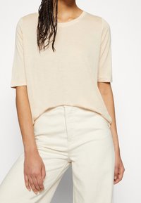 Jasnobeżowa koszulka z krótkim rękawem i okrągłym dekoltem, o miękkiej teksturze i luźnym kroju, zestawiona z białymi jeansami o wysokim stanie.