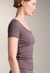 Top slim, cu mâne scurte, dintr-un material moale, ribetat. Dispune de un decolteu în V și o culoare mauve estompată, cu o textură netedă și părți fără cusături.