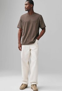 Tricou maro cu decolteu în V, pantaloni albi lejeri și pantofi de culoare maro deschis. Textură din bumbac moale; croială relaxată; design minimalist fără modele vizibile.