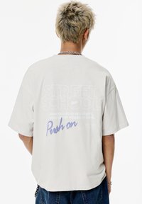 Vaaleanharmaa oversized t-paita, jossa on grafiikkateksti takana. Designissa on "STREET SCHOOL" ja lause "Push on" sinisellä.