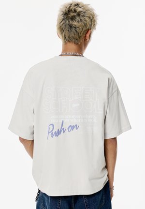 Svetlo sivé oversized tričko s grafickým textom na chrbte. Dizajn obsahuje "STREET SCHOOL" a frázu "Push on" v modrej farbe.