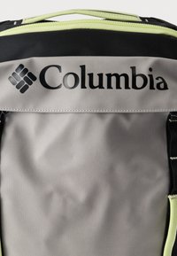 Κοντινή λήψη ενός γκρι και μαύρου σακιδίου Columbia με φερμουάρ lime green και κεντημένο λογότυπο στην μπροστινή πλευρά.