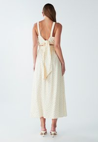 Vestido maxi sin mangas de color crema con lunares negros, diseño de espalda descubierta y cintura atada. Tela suave con una silueta fluida.