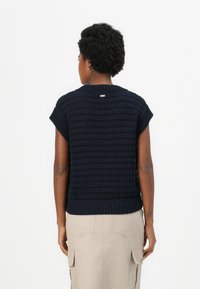 Dunkelblauer gestrickter Pullover mit kurzen Ärmeln, der ein strukturiertes Muster und einen gerippten Saum aufweist. Ein kleines Logotag ist auf der Rückseite sichtbar.