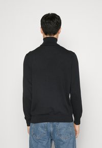 Svart polotröja i slät tyg, med långa ärmar och ribbade muddarna, parat med ljusblå denimjeans.