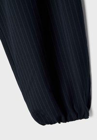 Marineblaue Nadelstreifen-Hosenbein aus Stoff mit elastischem Bündchen, dargestellt vor einem einfarbigen hellgrauen Hintergrund.