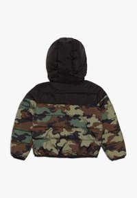 Polstret jakke med en sort øverste del og et camouflage-mønster i grøn, brun og sort. Inkluderer hætte og elastiske manchetter.